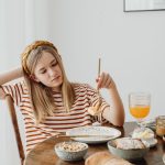 Teen girl in striped shirt at breakfast table with fruits, bread, and juice. Casual morning setting.